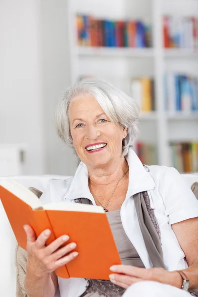 Seniorin hält Buch im Sitzen auf Sofa — Stockfoto