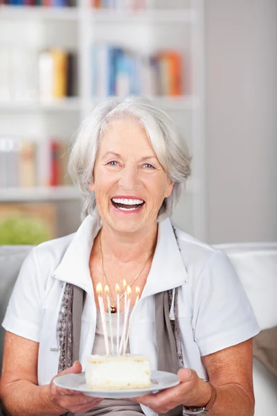 Laughing elderly woman holding a birthday cake — Stock Photo, Image