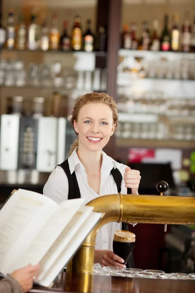 Smiling barmaid serving dark draft beer — Stock Photo, Image