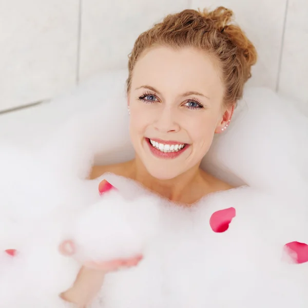 Mujer feliz disfrutando de un baño con espuma y pétalos —  Fotos de Stock