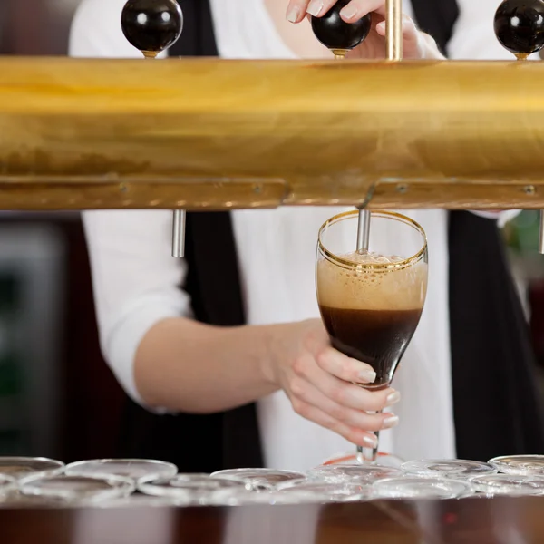 Kellnerin schenkt dunkles Bier ein — Stockfoto