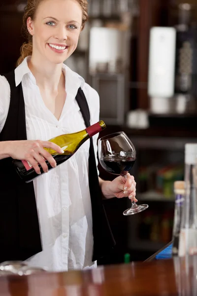 Glimlachend serveerster gieten een glas rode wijn — Stockfoto