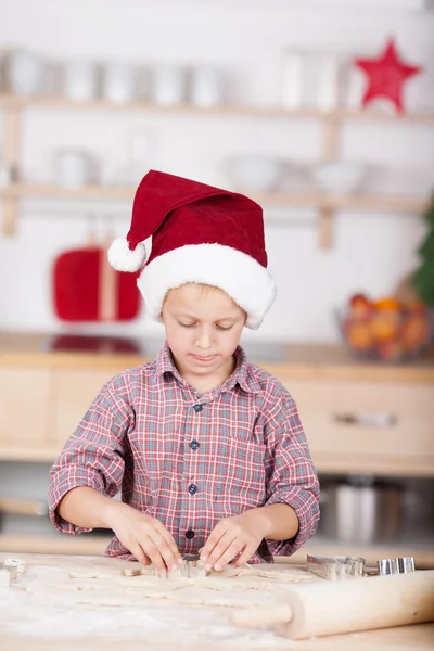 Milý chlapeček v kuchyni v červeném klobouku santa — Stock fotografie