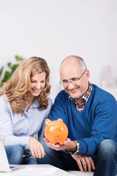 Paar staren naar hun piggy bank met een glimlach — Stockfoto