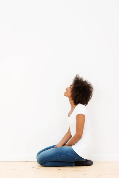 Femme agenouillée regardant un mur blanc — Photo