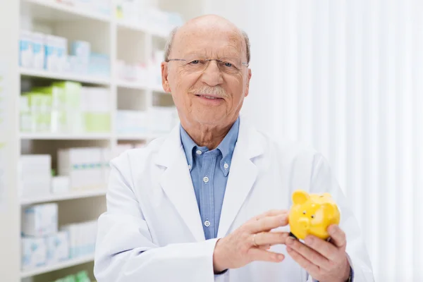 Smiling pharmacist holding a piggy bank — Stock Photo, Image