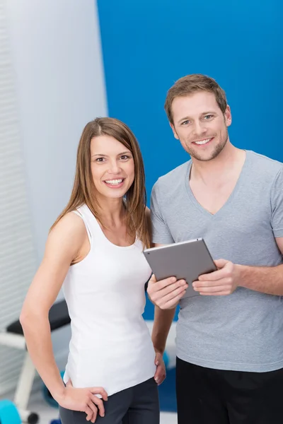 Pareja joven en el gimnasio monitoreando su ejercicio — Foto de Stock