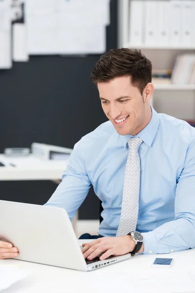 Geschäftsmann lächelt, während er an seinem Schreibtisch arbeitet — Stockfoto