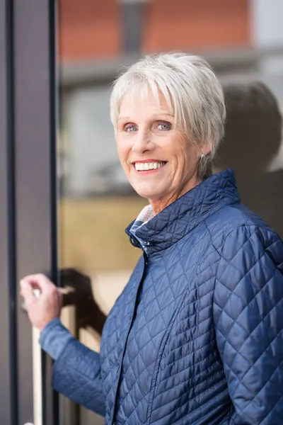 Smiling senior woman exiting her house — Stock Photo, Image