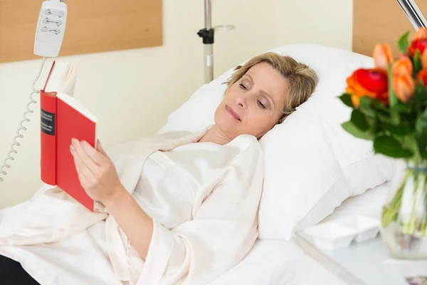 Woman lying in hospital reading a book — Stock Photo, Image