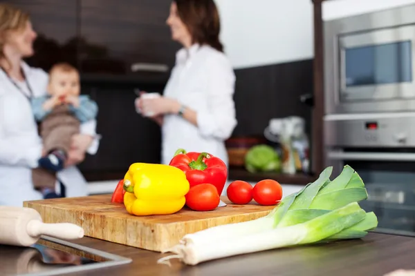 Vegetables and chopping board with women and baby — Stock Photo, Image