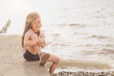 Çocuk deniz kenarında oturur ve günbatımının tadını çıkarır. Çocuklarla ilgili mesajlar için bir yer. Neşeli bir kız deniz havasının tadını çıkarıyor. Güneş ışınları çerçeveye düşer.