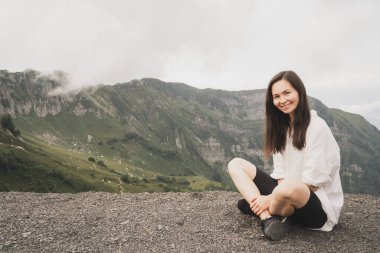 Dağlarda meditasyon yapan bir kız. Doğada Yoga İnzivası. Beyaz gömlekli bir kız güzel doğanın tadını çıkarır. Kız lotus pozisyonunda gözleri kapalı oturuyor..