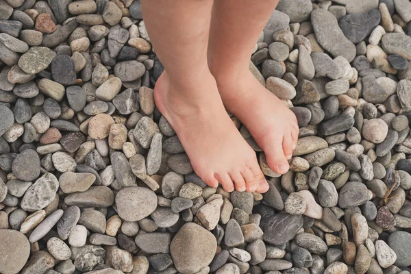 Lapos lábak megelőzése gyermekeknél. A gyermek mezítláb jár a köveken. A valgusz láb kezelése gyermekeknél és felnőtteknél. Közelkép a gyerekek lábáról a sziklákon. — Stock Fotó