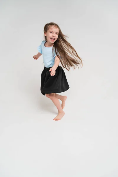 Маленькая и милая девочка радуется и танцует. Ребенок в голубой футболке и черной юбке. Ребёнок с очень длинными волосами. Счастливый ребенок на ярком фоне — стоковое фото