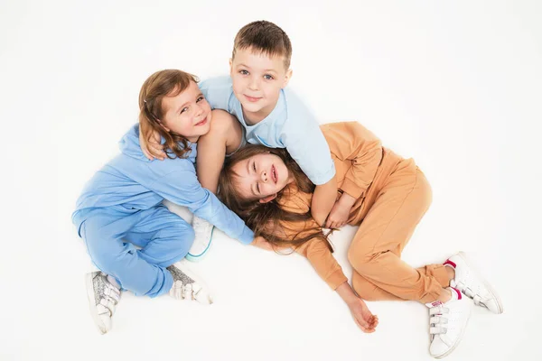 Дружелюбные дети играют вместе. Дети в монохромной одежде деликатного цвета. Спортивный образ жизни. Дети лежат на полу и обнимаются. — стоковое фото