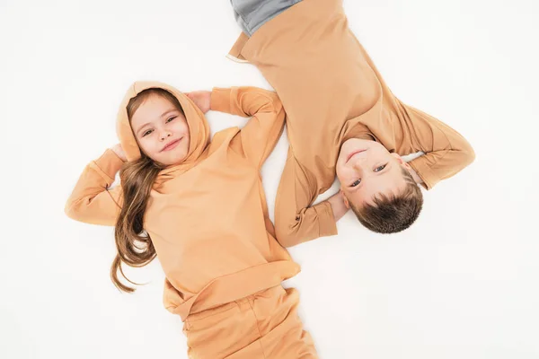 As crianças de sportswear deitam-se no chão e olham para a moldura. Amizade de um menino e uma menina desde a infância. O irmão e a irmã puseram as mãos atrás da cabeça e descansaram.. — Fotografia de Stock