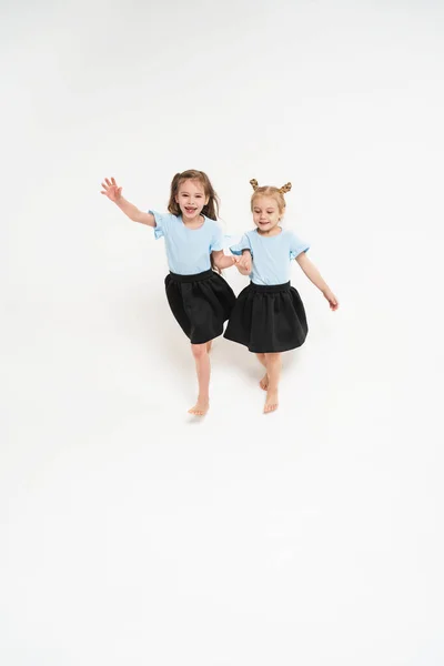 Two children are happily running. Happy and carefree childhood. Girls in identical T-shirts and skirts. The girl waves her hand and laughs. — стоковое фото