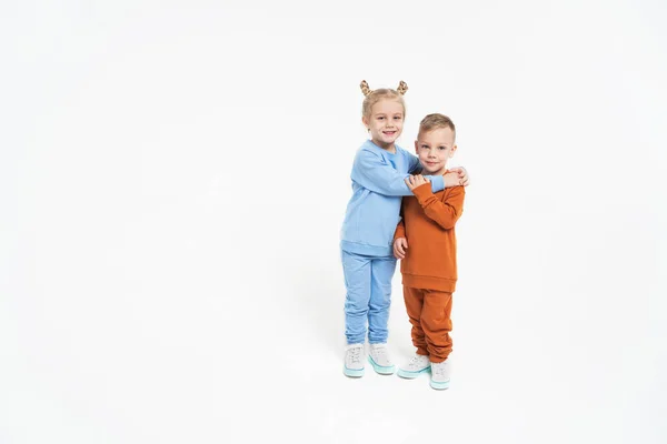 Маленькая девочка и обнимашки мальчика. Дети любят друг друга. На монохромном фоне, ребята в спортивной одежде. Синий спортивный костюм — стоковое фото