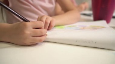Çocuk renkli kalemlerle resim çiziyor. Çocuğun yakın plan çizimleri. Pembe tişörtlü bir kız resim çiziyor.