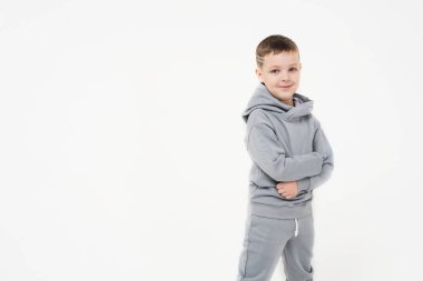 Gri eşofmanlı bir çocuk hafif arka planda duruyor. Mesaj ve reklam için bir yer. Çocuk ellerini bağladı ve bir şey bekliyor.