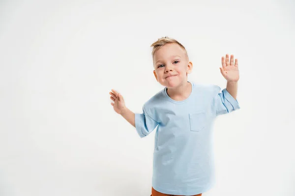 Un chico con una camiseta azul sobre un fondo monocromático. El chico se retuerce y baila. Un lugar para el texto sobre los niños. Niño alegre con el pelo rubio —  Fotos de Stock