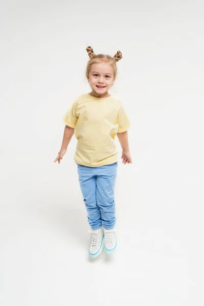 Девушка в спортивной одежде прыгает высоко. Ребенок в жёлтой футболке и синих штанах. Ребенок с светлыми волосами на монохромном фоне. — стоковое фото