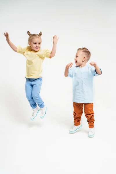 Вертикальное фото с детьми. Забавные дети прыгают и веселятся. Дети в спортивной одежде. Дружба с детства между мальчиком и девушкой. — стоковое фото