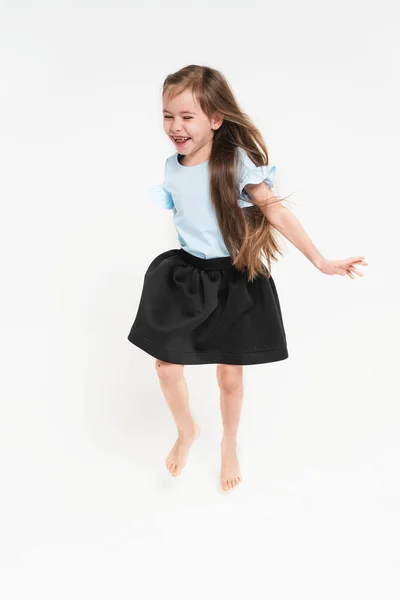 Девушка в голубой футболке и черной юбке. Маленькая школьница с длинными волосами. Девушка танцует и радуется. — стоковое фото