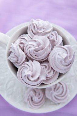 Lila renkli arka plan üzerinde beyaz bir çay fincanı içinde meringues