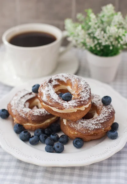 Puffs de creme ou choux anéis de pastelaria com mirtilos no prato — Fotografia de Stock