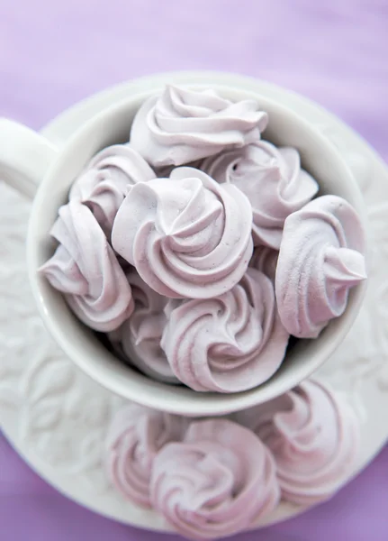 Meringhe in una tazza da tè bianca su uno sfondo di colore lilla — Foto Stock