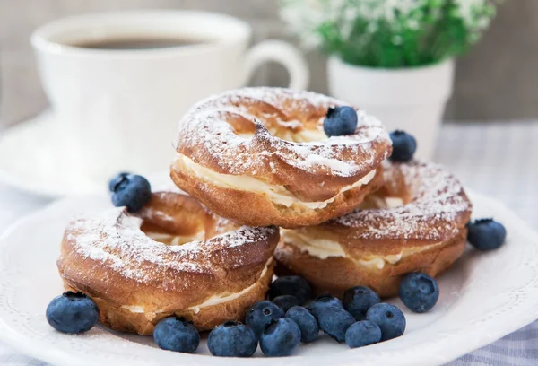 Sbuffi di panna o anelli di pasta choux con mirtilli sul piatto — Foto Stock