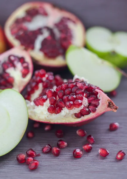 Pomegranate, pomegranate seeds and apple on a wooden board — Stock Photo, Image