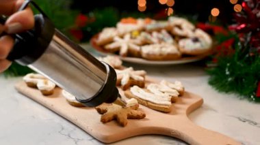Noel kurabiyelerini kar tanesi şeklinde beyaz kremayla süsleyen bir kadına yakın çekim. Noel şekerleriyle dolu mutfak masası. Geleneksel Noel hazırlıkları.