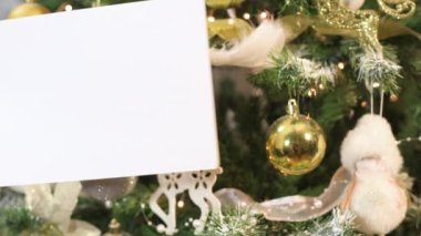 Güzel süslenmiş Noel ağacının önünde el ele tutuşan beyaz kağıt kart notu. 