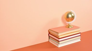 Altın Dünya küre, koyu ve parlak turuncu temalara karşı sıralı kitap yığınının üzerinde dönüyor. Hareketi durdur