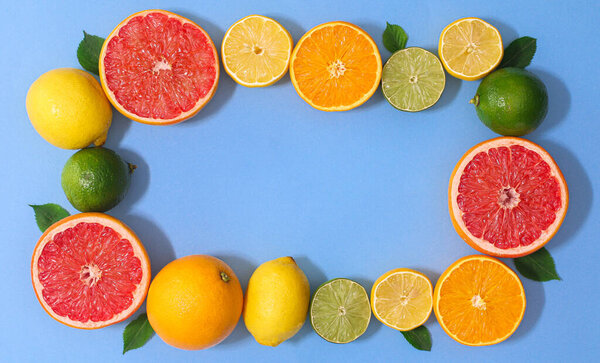 Creative copy space frame with various citrus fruits and green leaves on vibrant blue background. Flat lay summer border