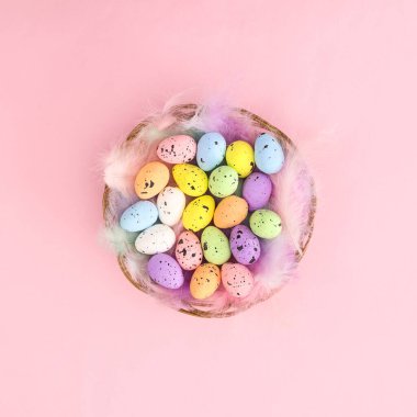 Tüylü ahşap sepet ve pastel parlak pembe arka planda renkli Paskalya yumurtaları. Sabit mevsim bahar tatili konsepti