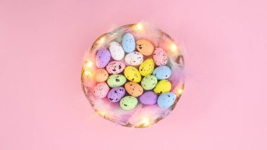 Tüylerle süslenmiş yaratıcı ahşap bir sepet ve pastel pembe arka planda Paskalya için renkli yumurtalar. Asgari bahar bileşimi