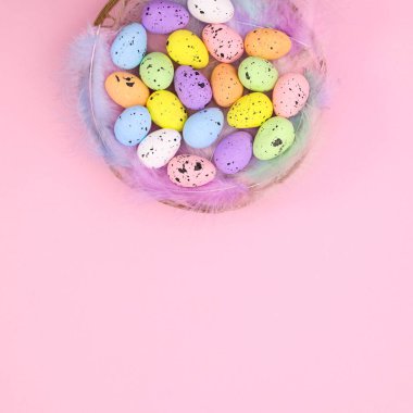 Paskalya tebrik kartı, üzerinde renkli yumurtalar ve pastel pembe arka planda tüyler olan ahşap bir sepet. Dümdüz uzanır