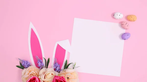 春休みはパステルピンクの背景に花で飾られたウサギの耳で創造的な紙のカードコピースペース 創造的なイースターの概念 ロイヤリティフリーのストック画像
