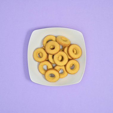 Pastel mor arka planda beyaz tabakta tatlı kurabiyeler. Düz konsept yemek.