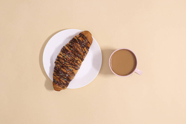 Шоколадный круассан на тарелке с горячим кофе на пастель бежевый backgorund. Концепция вкусной закуски и сладкой пищи
