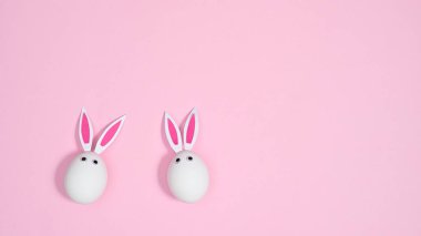 Pastel pembe arka planda tavşan kulaklı beyaz yumurtalar. Düz konsept çok az yaratıcıydı. Paskalya tatili