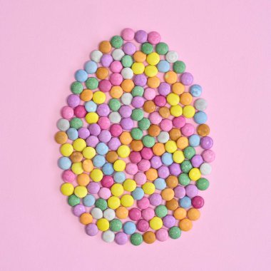 Pastel pembe arka planda renkli şekerlerle yapılmış yaratıcı Paskalya yumurtası. Düz Paskalya konsepti