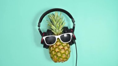 Güneş gözlüklü ve kulaklıklı yaratıcı ananas mavi arka planda dans ediyor. Dur hareketi düz yatıyordu