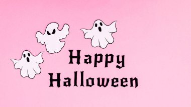 Happy Halloween text with ghosts on pastel pink background. Flat lay