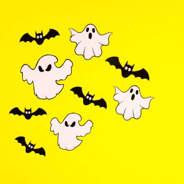 Halloween ghosts and bats on vibrant yellow background. Autumn holidays. Flat lay creative concept