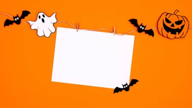 Creative paper card copy space hanged on rope with scary stickers for Halloween on orange background. Flat lay